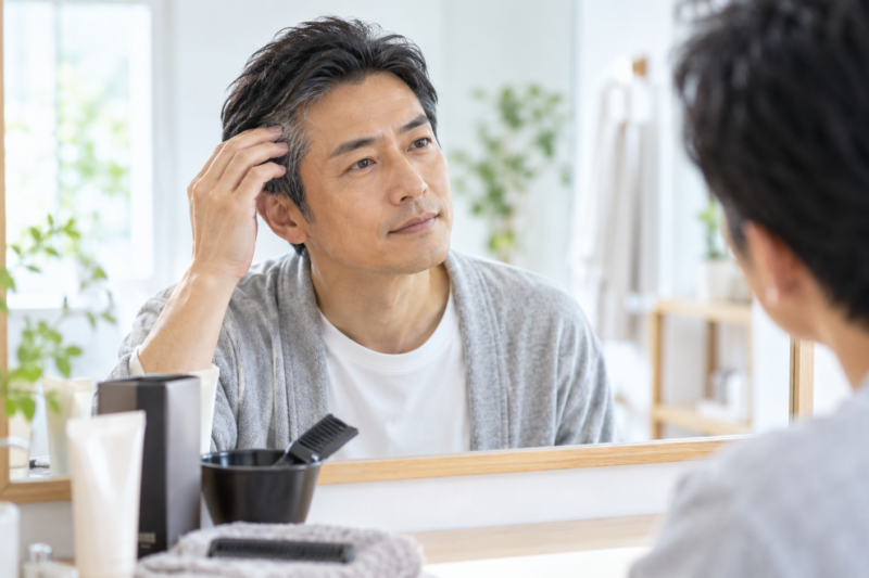 鏡の前でこめかみの白髪を確認する男性