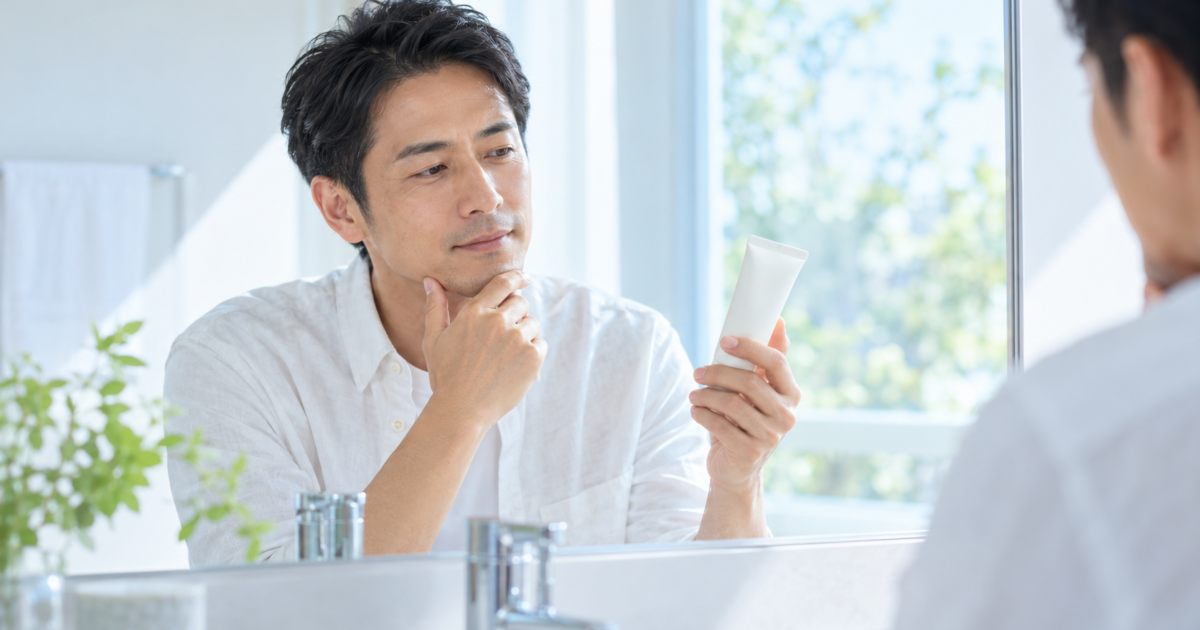 顔用の日焼け止めを手に取り鏡の前で確認する男性