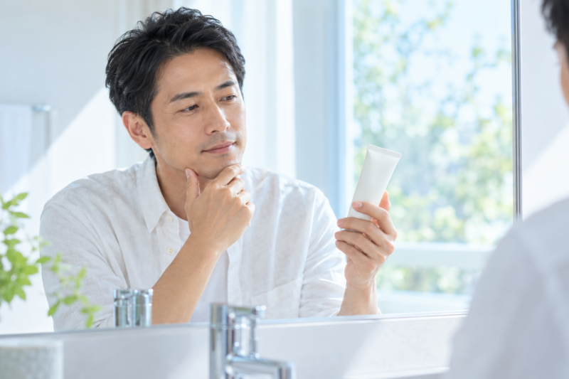 顔用の日焼け止めを手に取り鏡の前で確認する男性